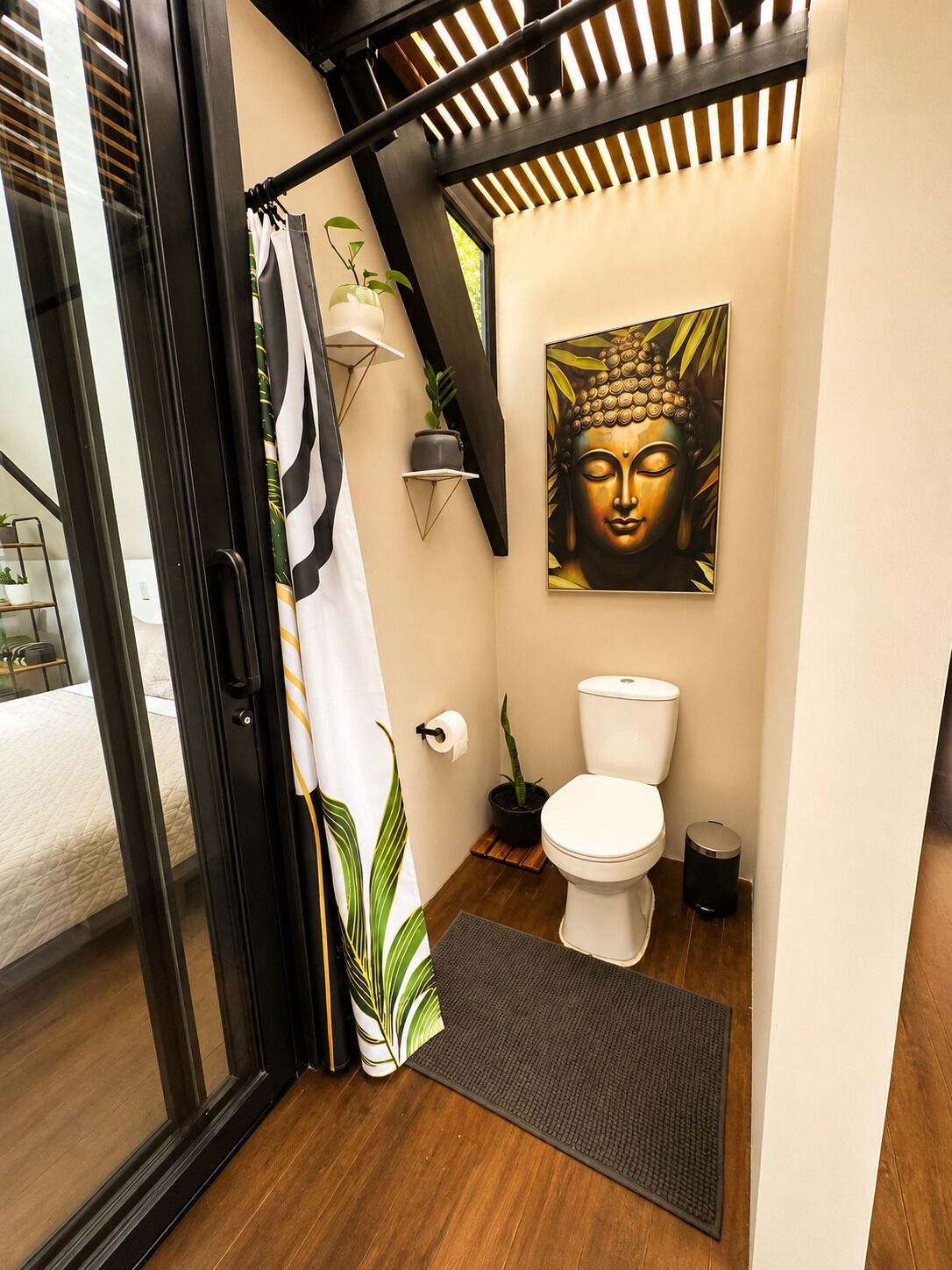 A modern bathroom with a toilet, a shower curtain, a Buddha painting, and a small potted plant.