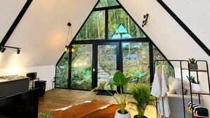 A modern loft bedroom with a sloped ceiling, large windows, a flat-screen TV, a wooden floor, and a cowhide rug. - The Naked Jungle Luxury A-Frame w/ Mountain View (La Pinuela)
