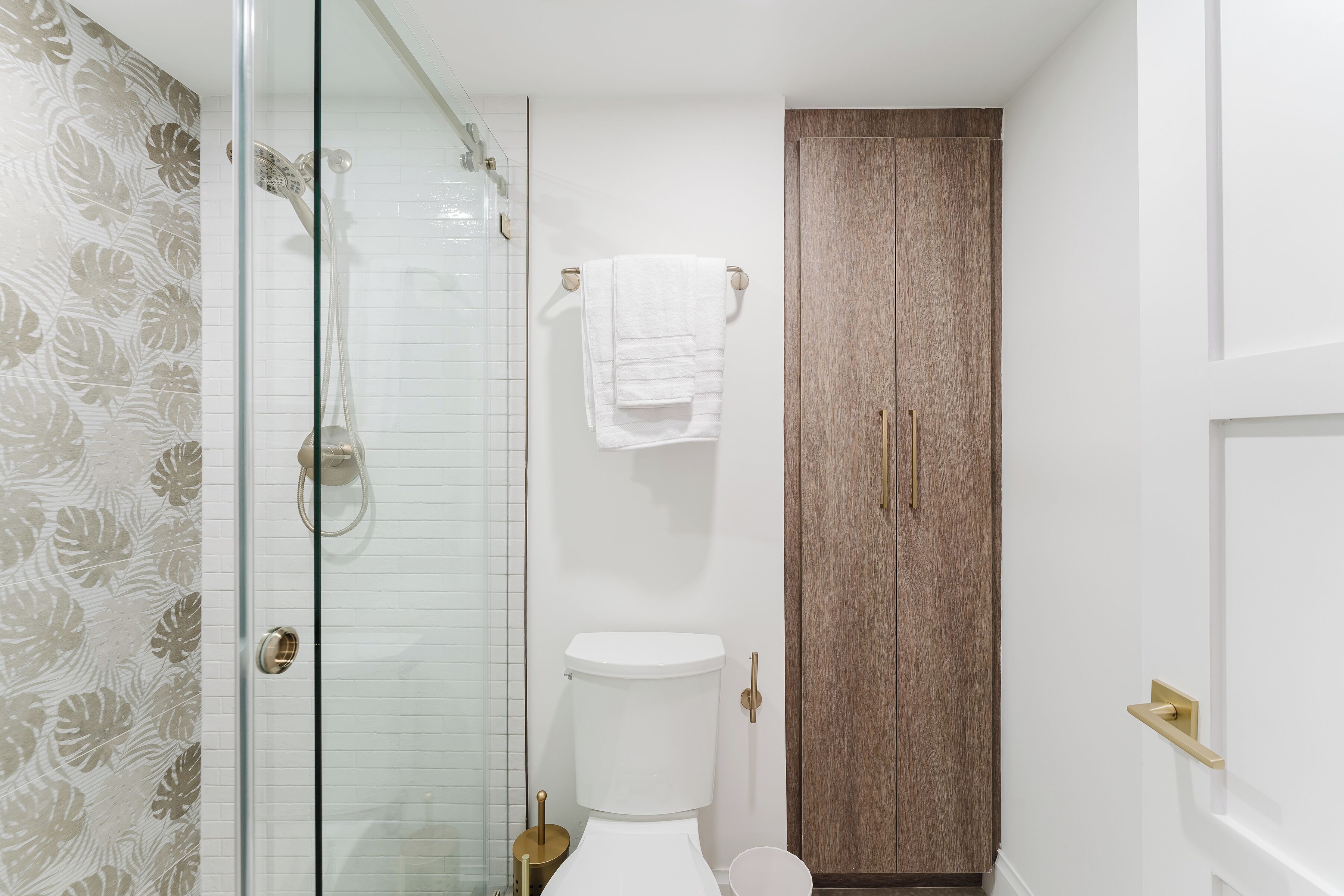 A bathroom with a glass shower enclosure, a toilet, and a wooden cabinet.