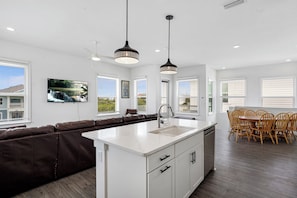 Una cocina moderna con una isla grande, muebles blancos y un comedor con sillas de madera.