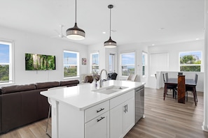 Una cocina moderna con una isla central, armarios blancos y un comedor con una mesa y sillas de madera.