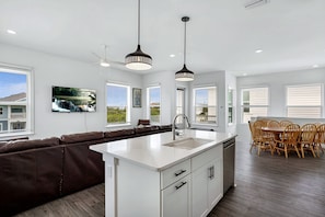 A modern kitchen with a central island, a dining area with wooden chairs, and a large window with a view of the outside. - Grand Vilano Compound: 18 Guests, 2 Pools (St. Augustine)
