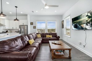 A modern kitchen with a stainless steel refrigerator, a dining area with a brown leather couch and a wooden coffee table, and a large window with a view of the outdoors. - Grand Vilano Compound: 18 Guests, 2 Pools (St. Augustine)