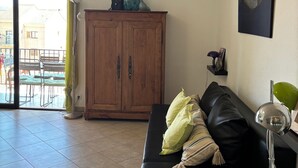 En stue med en sort lædersofa, et træskab, en gulvlampe samt et spiseområde med stole og bord.