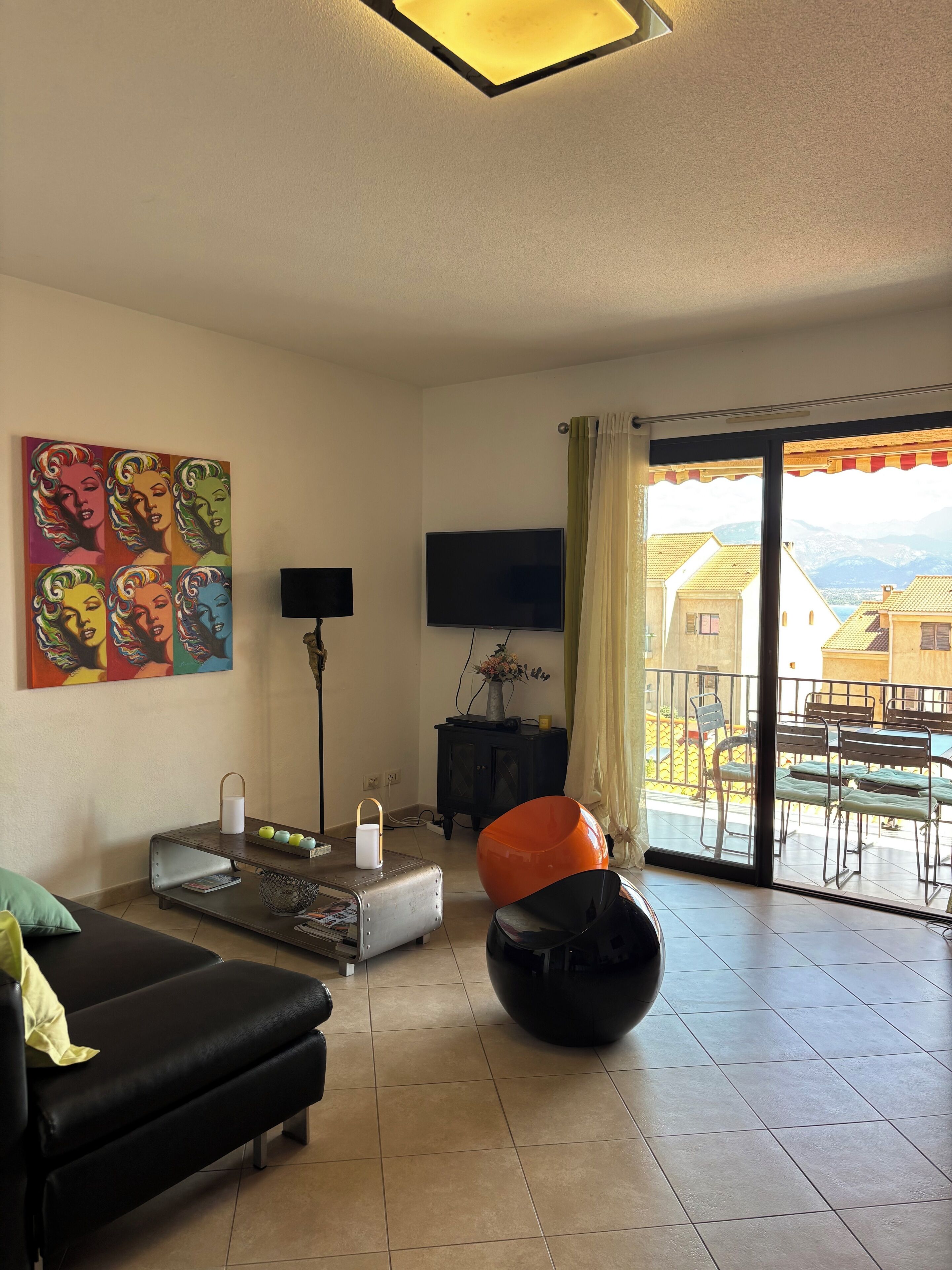 Uma sala de estar com um sofá, uma poltrona preta, uma mesa com abajur, uma televisão e um quadro na parede.