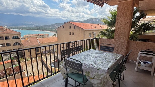 En balkon med et bord og stole, havudsigt og bygninger, samt et flisegulv.