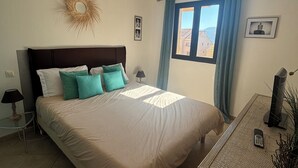 Et soveværelse med en seng, et natbord, en lampe, et vindue med gardiner, en vægdekoration og en loftlampe.