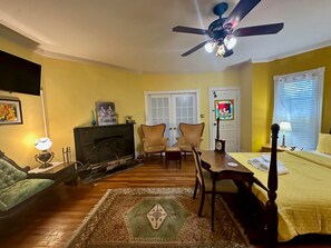 A room with a fireplace, a ceiling fan, a dining table with chairs, a bed, and a window with blinds. - The Gold Room/Spacious Victorian Inn (Gaithersburg)