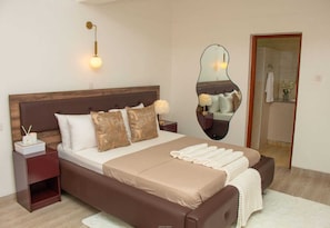 Une chambre à coucher avec un grand lit, une table de chevet avec une lampe, un miroir et une tête de lit en bois.