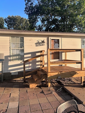 A mobile home with a wooden deck, a window with a metal grill, and a small porch area.