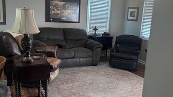 A living room with a sofa, armchair, rug, lamp, and ceiling fan.