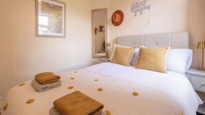 Un lit bien fait, avec une couette blanche et beige, un miroir, un élément de décoration murale et une lampe de chevet.