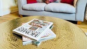 Un salon avec un canapé gris, des coussins rouges, un magazine posé sur une table basse à texture et des œuvres d’art accrochées au mur.