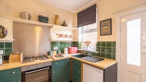 Une cuisine compacte équipée d’une cuisinière à gaz, d’un four et d’un évier. On y trouve des armoires vertes, un petit plan de travail et une fenêtre avec vue.