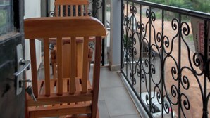 Un balcon avec une chaise en bois, une rambarde en métal et une vue sur des bâtiments situés au loin.