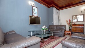 Un salon avec des canapés en cuir, une table basse en verre, un téléviseur à écran plat, un meuble en bois et un miroir décoratif.
