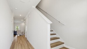 A hallway with wooden flooring, white walls, and a staircase with wooden steps and white railings. - Lost Bay Hideaway | Garden View (Orange Beach)
