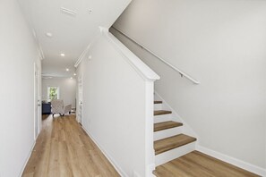 Ein Flur mit Holzboden, weißen Wänden und einer Treppe mit Holzstufen und weißen Geländern.