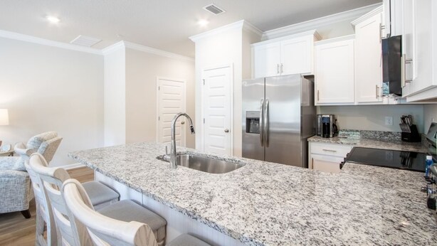 A kitchen with granite countertops, stainless steel appliances, white cabinetry, and a bar area with bar stools. - Lost Bay Hideaway | Garden View (Orange Beach)