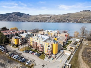 A multi-story residential building with a parking lot and a lake in the background.