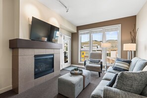 A living room with a fireplace, a sofa, a chair, and a television on the wall. - Welcome to Lakeside Lookout – your easy, lakeside, Okanagan getaway. (Vernon)