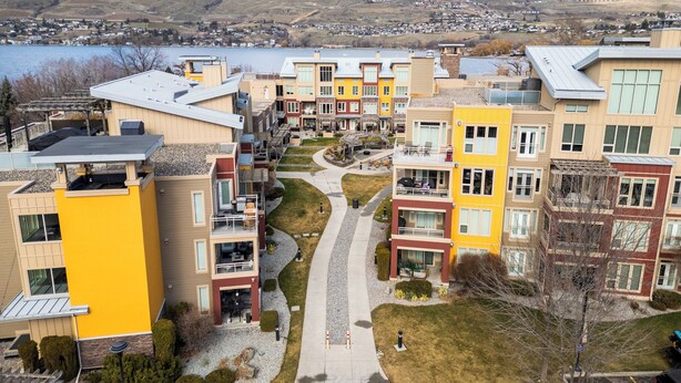 A residential area with modern apartment buildings, a central walkway, and a lake in the background. - Welcome to Lakeside Lookout – your easy, lakeside, Okanagan getaway. (Vernon)