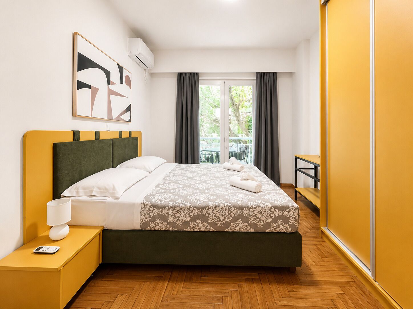 A hotel room with a bed, bedside table, and a view of greenery outside.