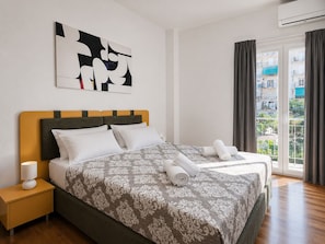 A hotel room with a bed, a nightstand, a window with curtains, and a view of buildings. - Athens City Escape - 2 BDRM Apartment (Athina)