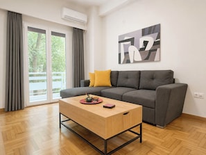 A modern living room with a grey sofa, a wooden coffee table, and a large abstract painting on the wall. - Athens City Escape - 2 BDRM Apartment (Athina)
