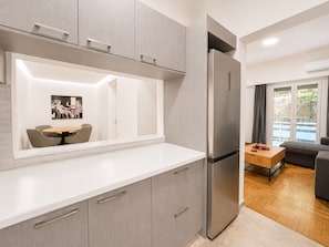 A modern kitchen with grey cabinets, a stainless steel refrigerator, a dining area with a table and chairs, and a view of a balcony. - Athens City Escape - 2 BDRM Apartment (Athina)