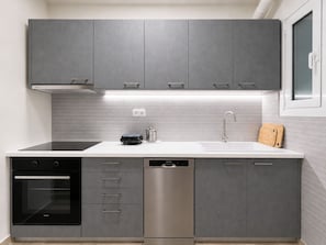 A modern kitchen with grey cabinets, a stainless steel dishwasher, a black oven, and a white countertop. - Athens City Escape - 2 BDRM Apartment (Athina)
