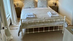 Ein ordentlich eingerichtetes Schlafzimmer mit einem Bett, zwei Nachttischen, einem an der Wand befestigten Spiegel und einer mit Vorhängen versehenen Tür.