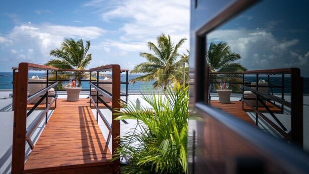 A wooden deck with a railing, palm trees, and a view of the ocean. - Ocean View! Jacuzzi! Outdoor Living! Centrally Located! (Arecibo)
