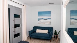 A room with a blue sofa, a door, a small plant, and two paintings on the wall. - Ocean View! Jacuzzi! Outdoor Living! Centrally Located! (Arecibo)