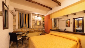 Ein Zimmer mit einem Bett, einem Schreibtisch, einem Stuhl, einem Spiegel und einer Steinwand mit einem Fenster.