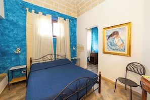 A bedroom with a bed, a chair, a nightstand, a painting, and a bathroom visible through an open door. - At the Frantoio | Nature, relaxation and Sicilian tradition just minutes from the sea (Valderice)