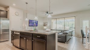 A modern kitchen with dark cabinets, a granite countertop, and pendant lighting. - 5BR Solterra Home Near Disney With Pool (Davenport)