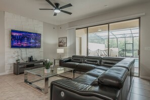 Ein modernes Wohnzimmer mit einem Ecksofa, einem Glastisch, einem Flachbildfernseher und einem Deckenventilator.