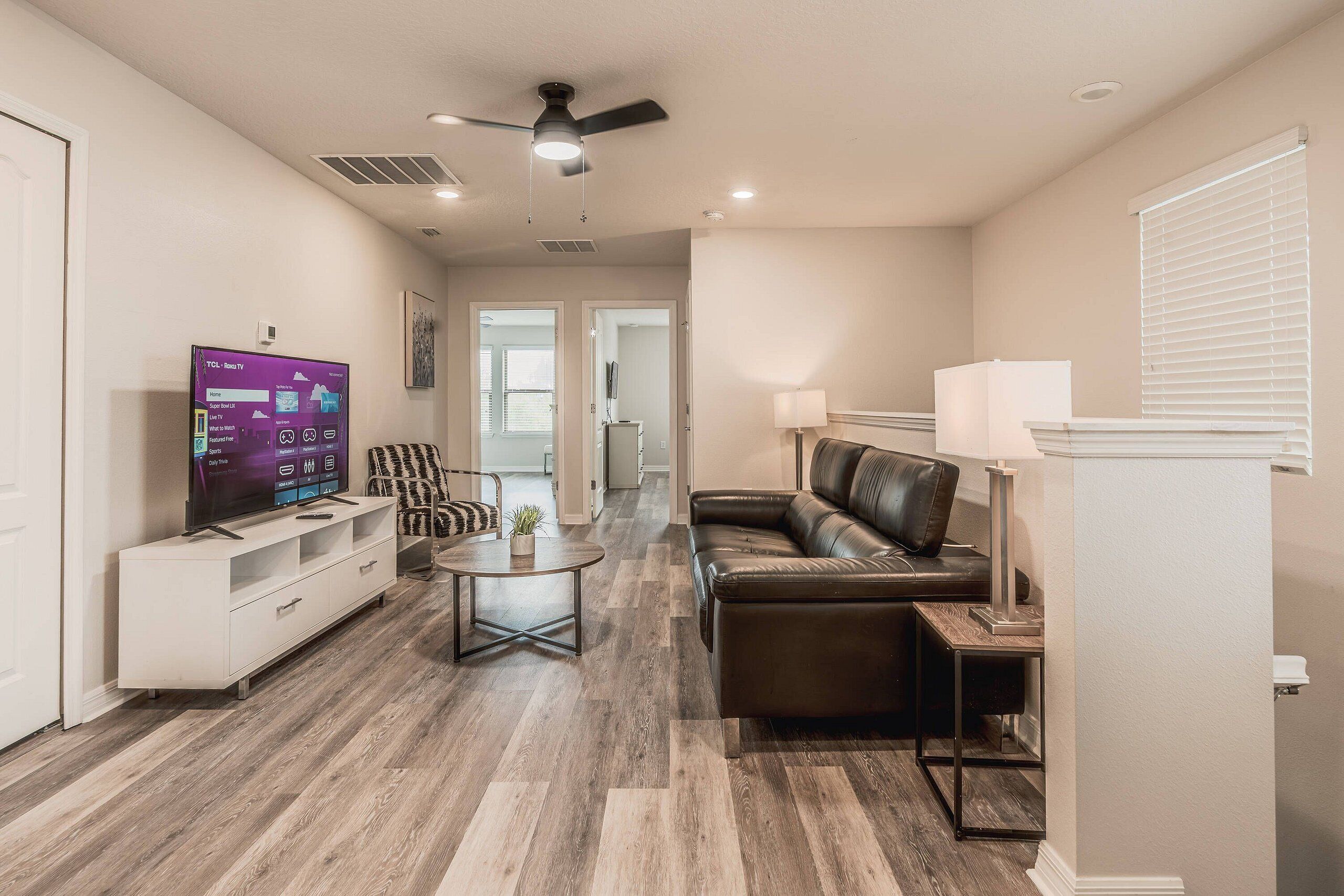 A modern living room with a TV, leather sofa, white entertainment unit, and a ceiling fan.