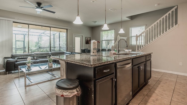 A modern kitchen with granite countertops, a black island, and a dining area with a glass table. - 5BR Solterra Home Near Disney With Pool (Davenport)