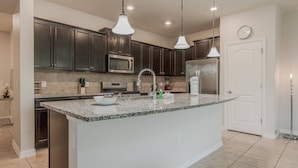 A kitchen with dark cabinets, a granite countertop, stainless steel appliances, and pendant lighting. - 5BR Solterra Home Near Disney With Pool (Davenport)
