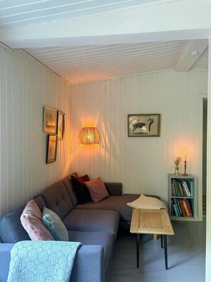 A living room with a sectional sofa, a coffee table, a bookshelf, and wall-mounted lamps. - Cozy holiday home near Tisvilde Hegn (Tibirke Sand, Frederiksværk)