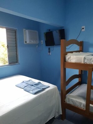 Ein Schlafzimmer mit Etagenbetten, einem Einzelbett, einem Fenster mit Jalousien, einer Klimaanlage, einem Fernseher und einer Steckdose an der Wand.