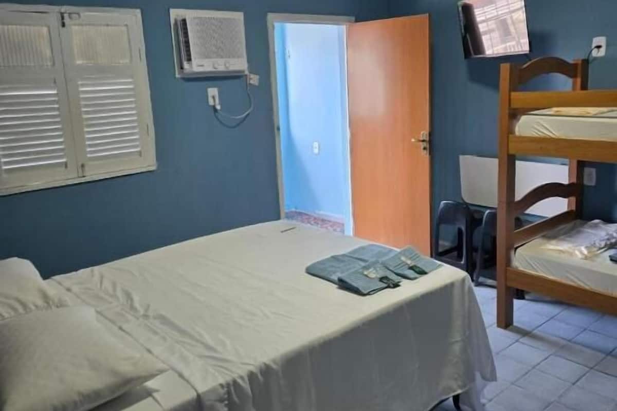 Una habitación con una cama, una litera, una puerta y un aire acondicionado instalado en la pared.