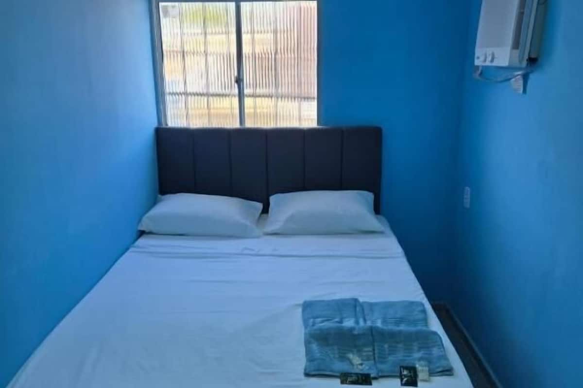 Una habitación con una cama, un ventanal con persianas y un aire acondicionado de pared.