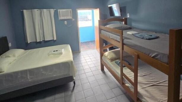 A dormitory room with two bunk beds, a television on the upper bunk, a window with curtains, and a door leading outside. - Pousada Hostel Beach Pajuçara (Maceió)