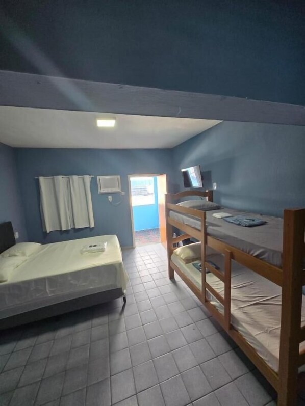 Habitación de residencia estudiantil con dos literas, un televisor en la litera superior, una ventana con cortinas y una puerta que da al exterior.