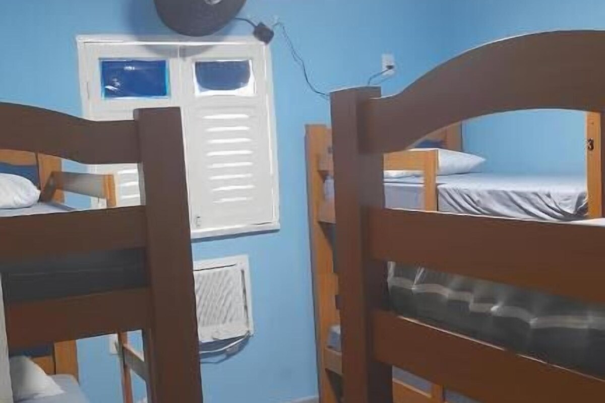 A room with bunk beds, a window with blinds, a wall-mounted air conditioner, and a ceiling light.