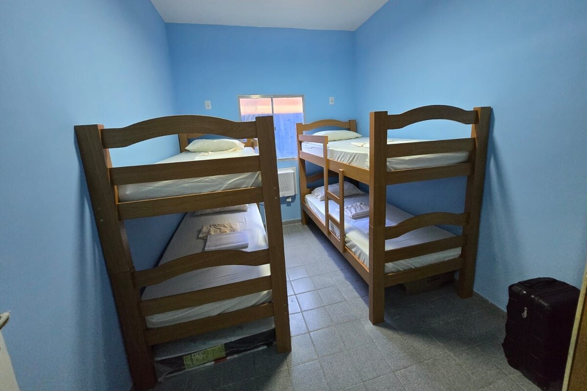 A room with two bunk beds, a window with blinds, a radiator, and a suitcase.