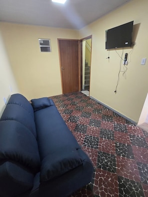 A room with a sofa, a door, a staircase, and a TV mounted on the wall. - Pousada Hostel Beach Pajuçara (Maceió)